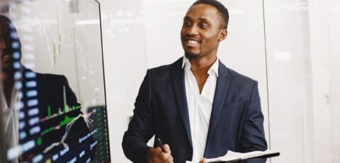 African man in a black suit. Big TV screen. Guy shows presentation.
